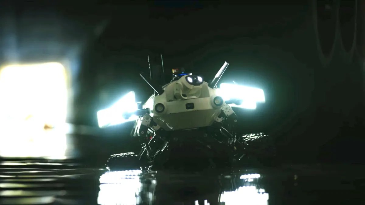 A white robot with wheels and lights on either side, the robot is in a dark, wet environment.